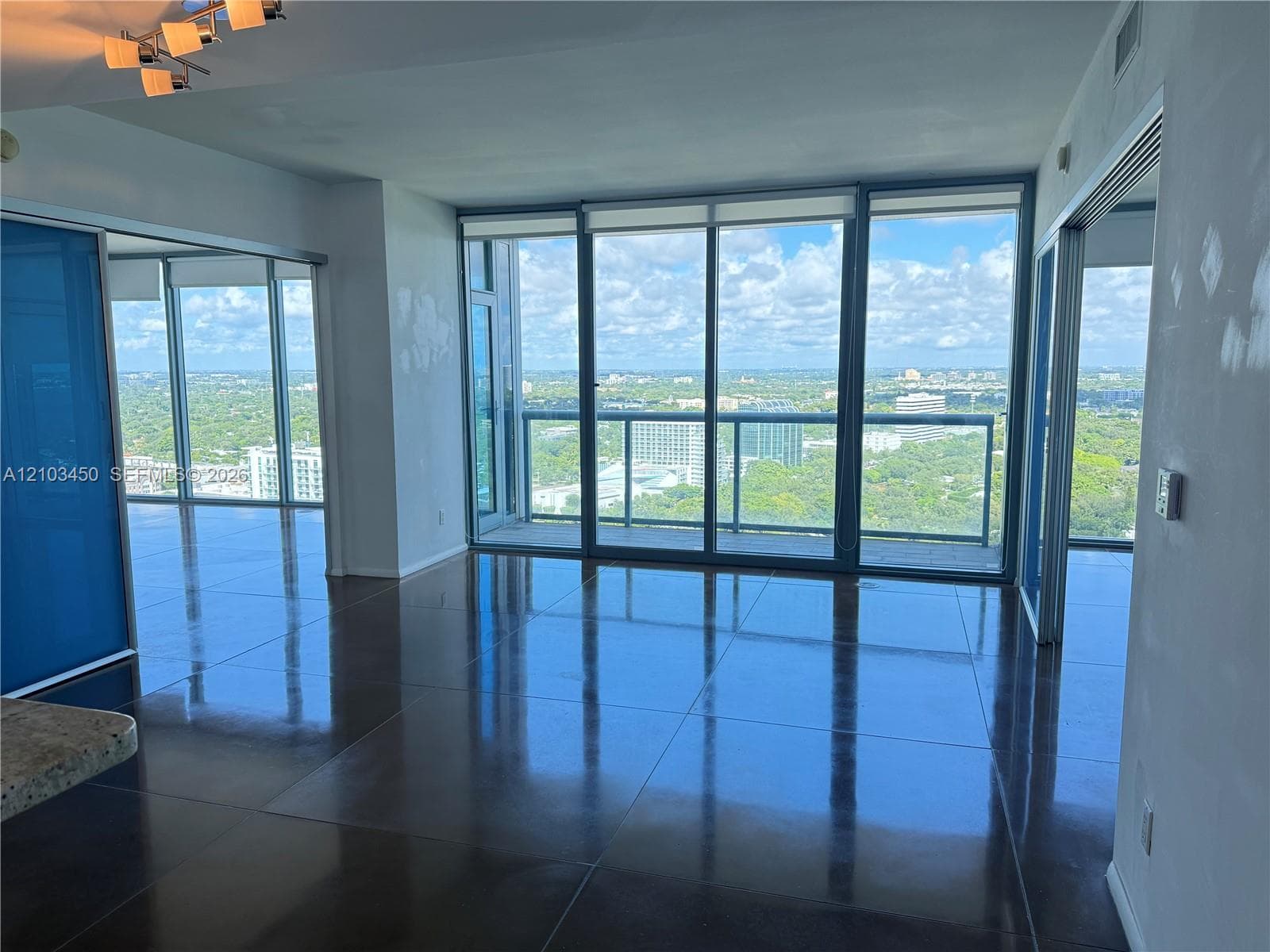 Floor-to-ceiling glass windows, polished tile flooring, metallic track lighting, and a glass-paneled balcony