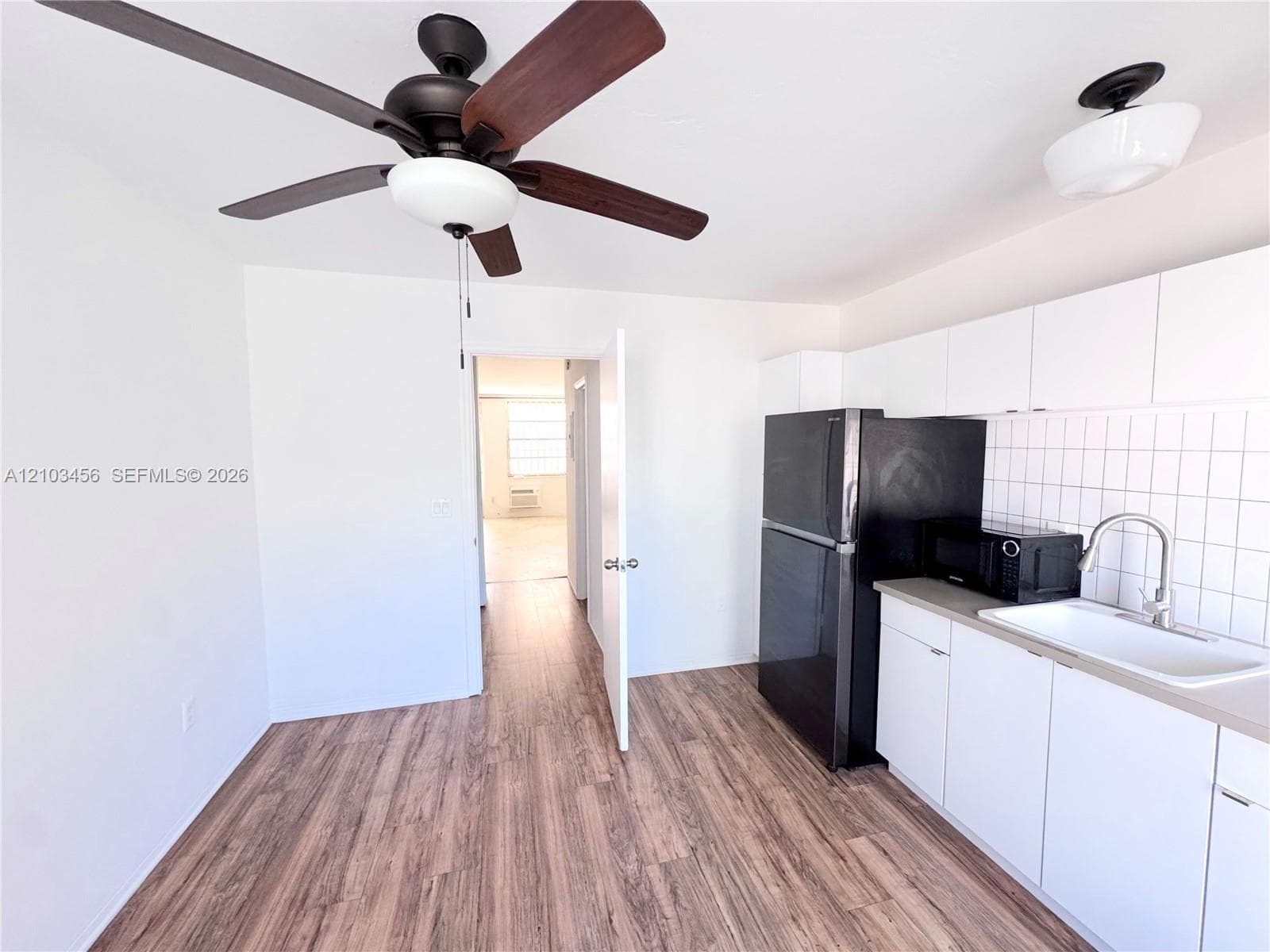 Kitchen featuring wood-finish flooring, white cabinetry, a square-tile backsplash, and a ceiling fan with integrated lighting