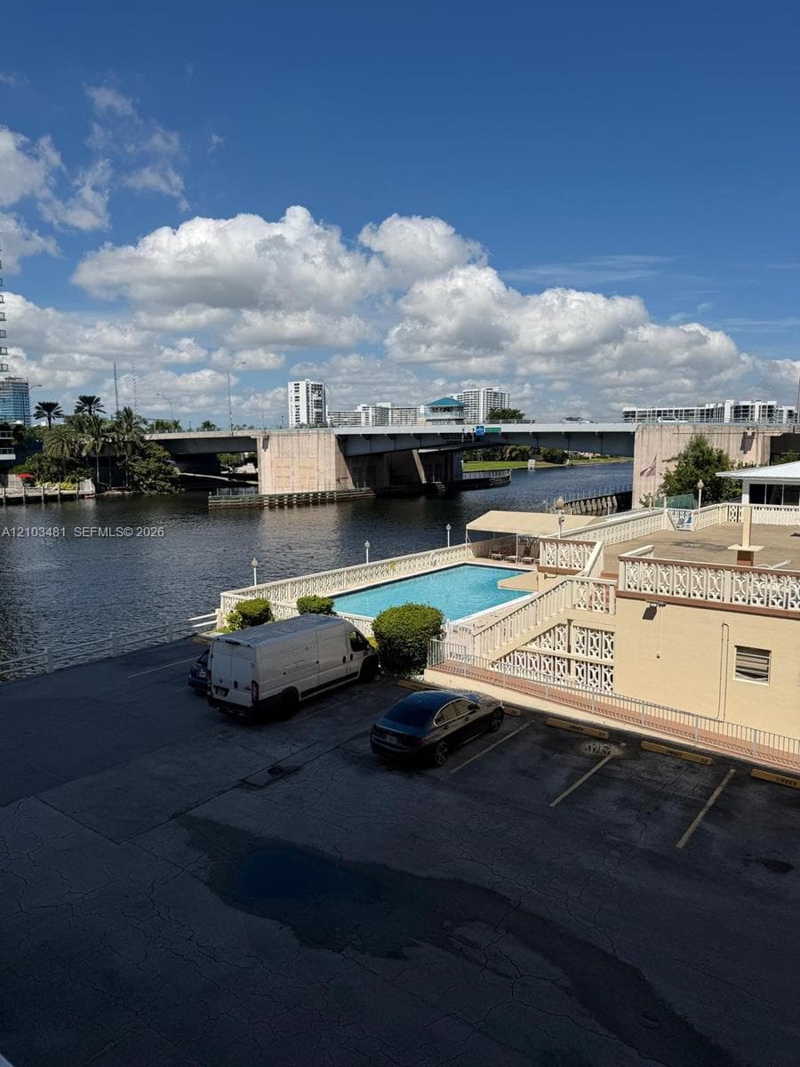 Waterfront property featuring an in-ground swimming pool, decorative balustrade railings, and paved parking area