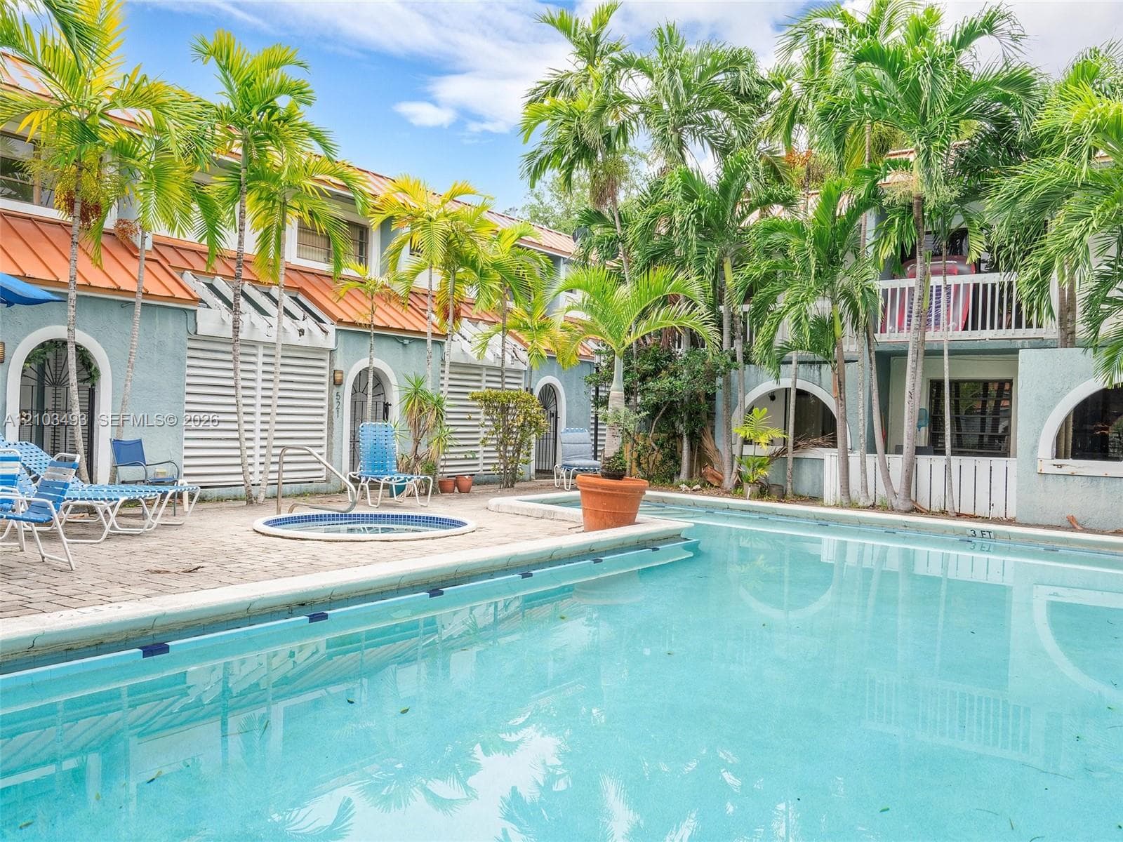 Swimming pool with integrated spa, paver patio, palm tree landscaping, and metal roof accents