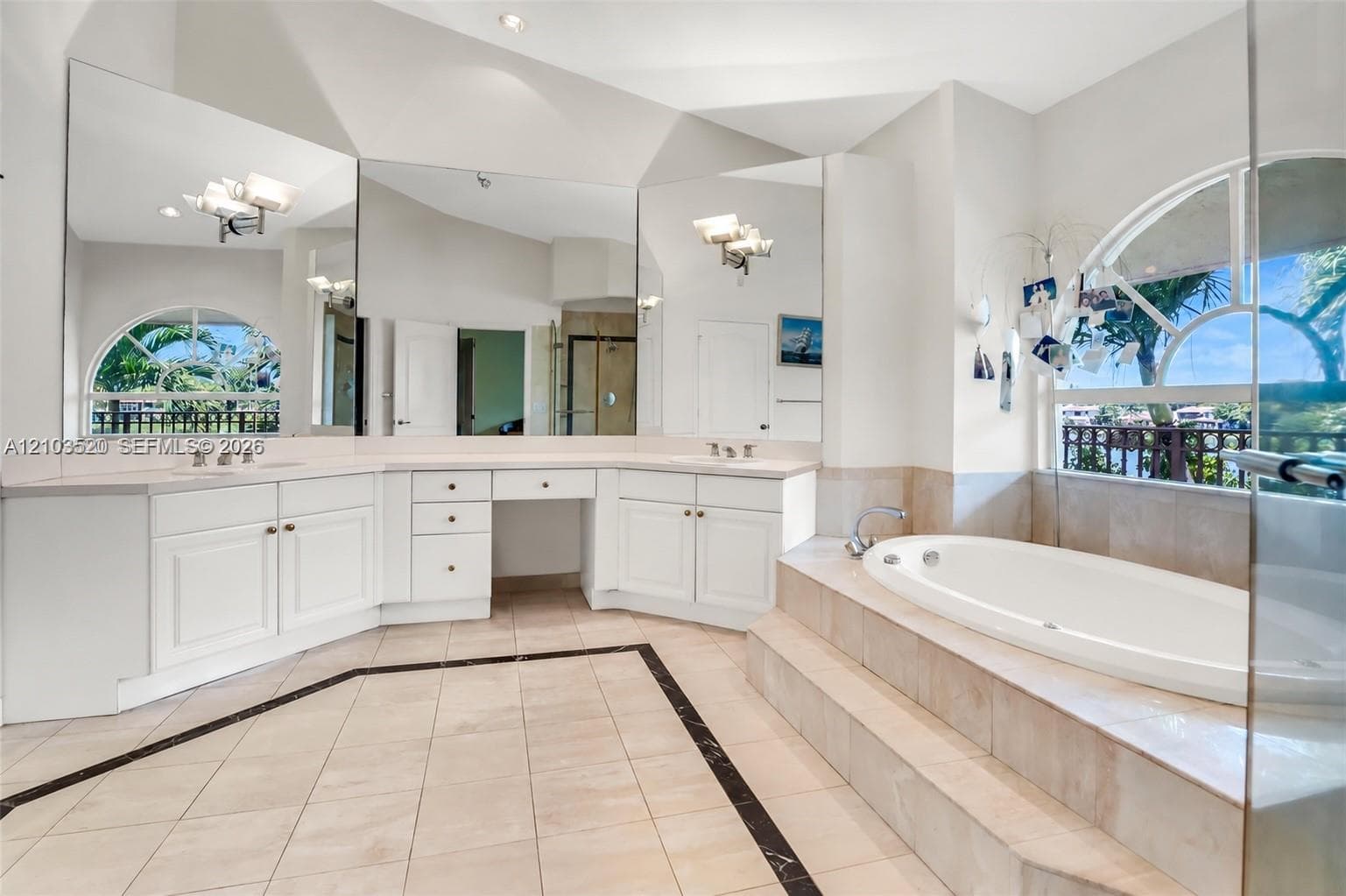 Bathroom featuring a dual-sink vanity with built-in cabinetry, an arched window, a raised soaking tub, and floor-to-ceiling mirrors