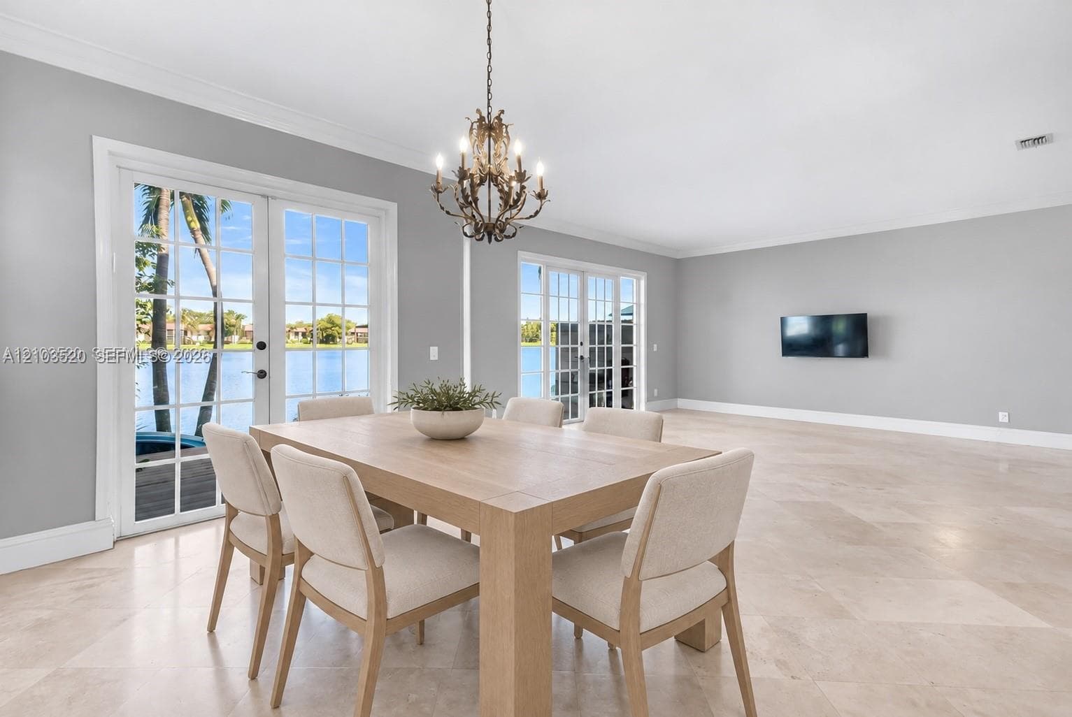 Large-format tile flooring, dual sets of multi-pane French doors, and an ornate wrought-iron chandelier