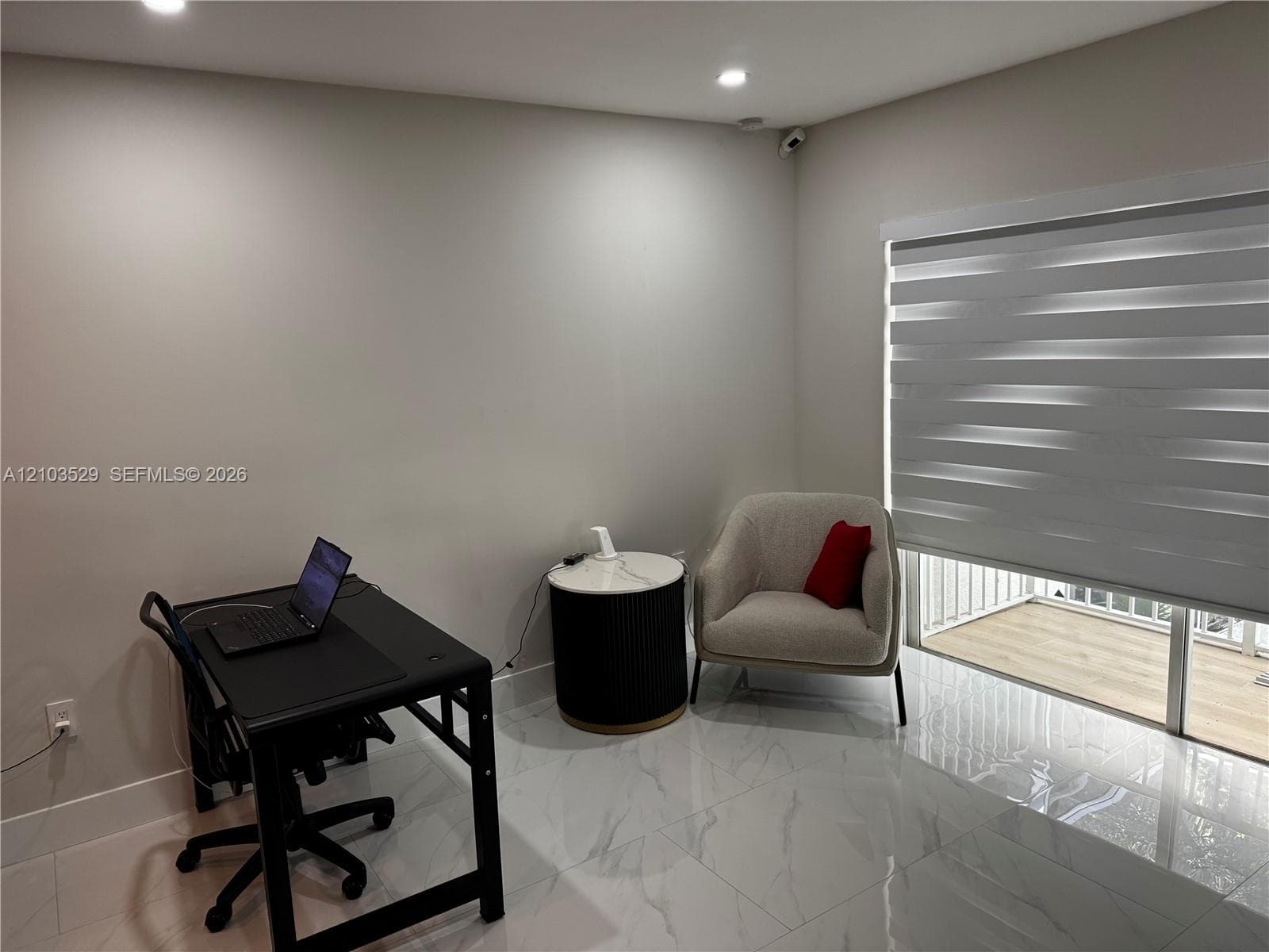Light-filled room featuring large-format polished stone-finish floor tiling, recessed lighting, and dual-layer privacy window treatments with direct access to an exterior balcony