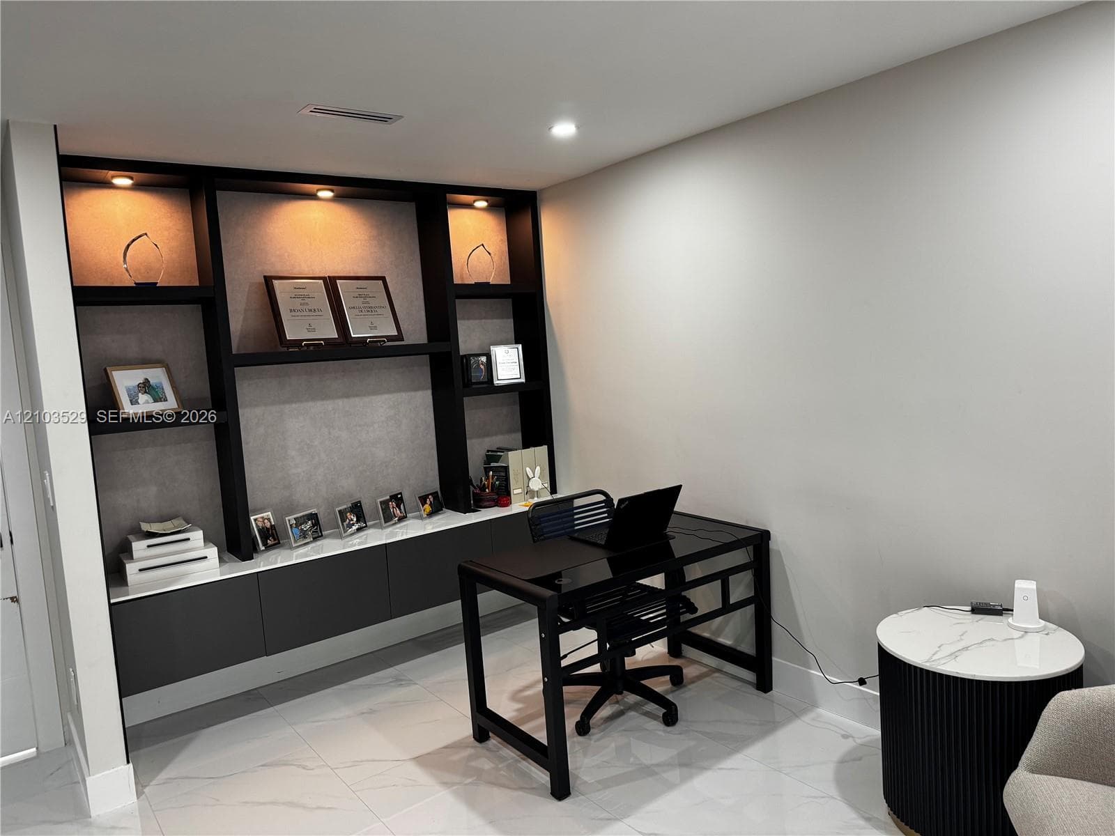 Built-in floor-to-ceiling shelving unit featuring integrated recessed lighting, stone-textured backing, and custom cabinetry with matte finish doors, complemented by large-format polished tile flooring