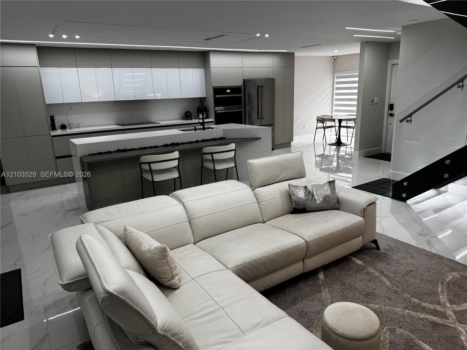 Contemporary kitchen featuring flat-panel cabinetry, a central island with a waterfall edge, large-format tile flooring, and integrated stainless steel appliances