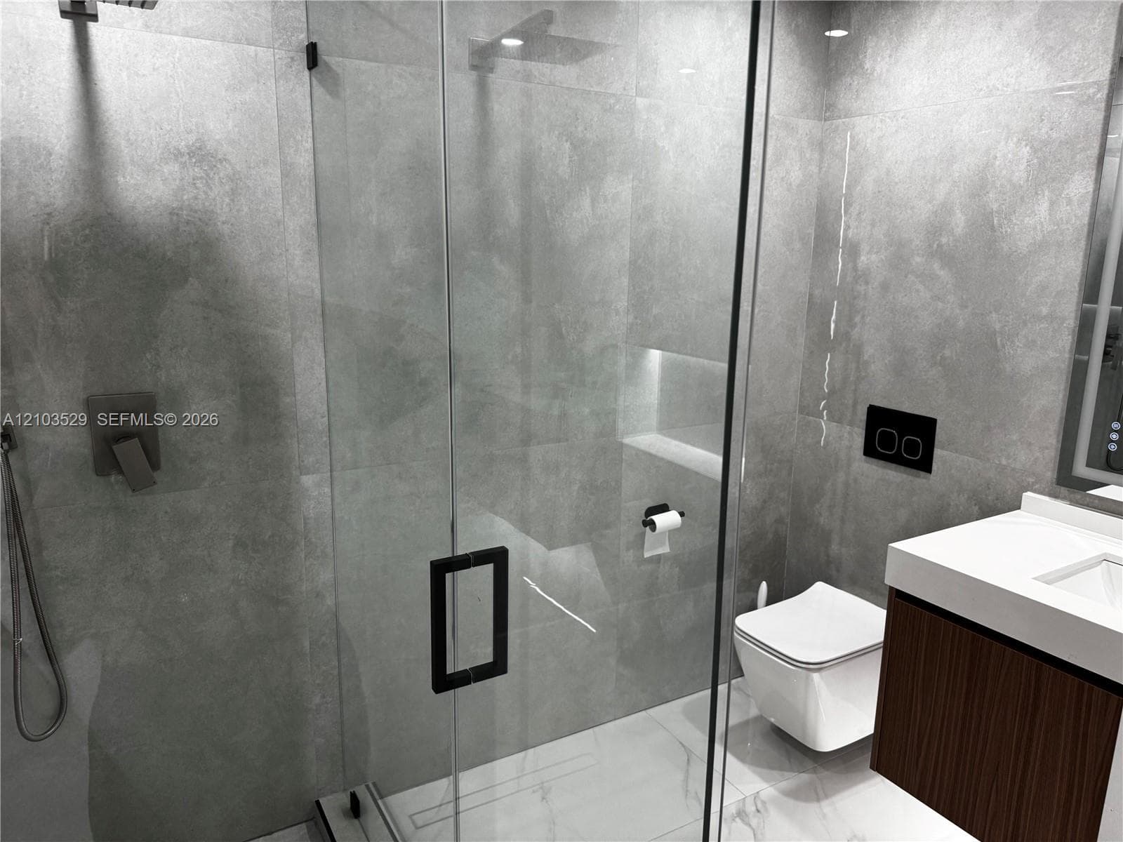 Walk-in shower with floor-to-ceiling stone-finish tile, glass enclosure, and wall-mounted plumbing fixtures, paired with a wall-hung toilet and floating vanity featuring a quartz countertop