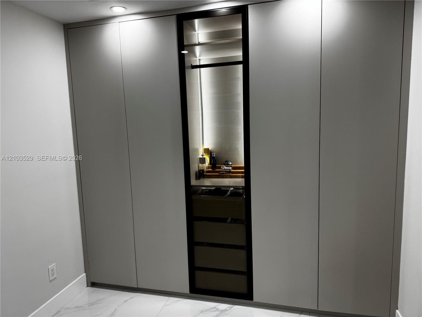 Floor-to-ceiling built-in cabinetry featuring matte-finish paneling, a central glass-front display section, integrated interior illumination, and internal pull-out storage drawers