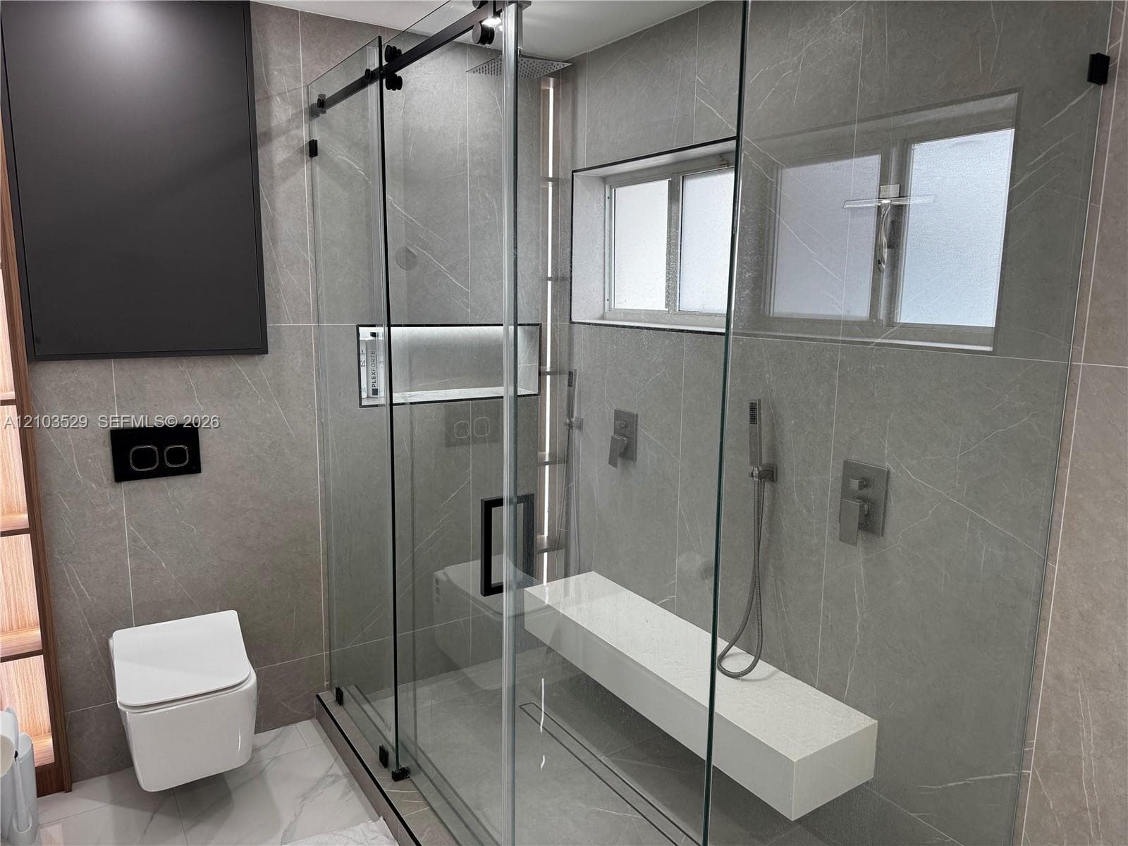 Walk-in glass-enclosed shower featuring large-format tile surround, integrated bench seat, handheld shower fixture, and recessed wall niche