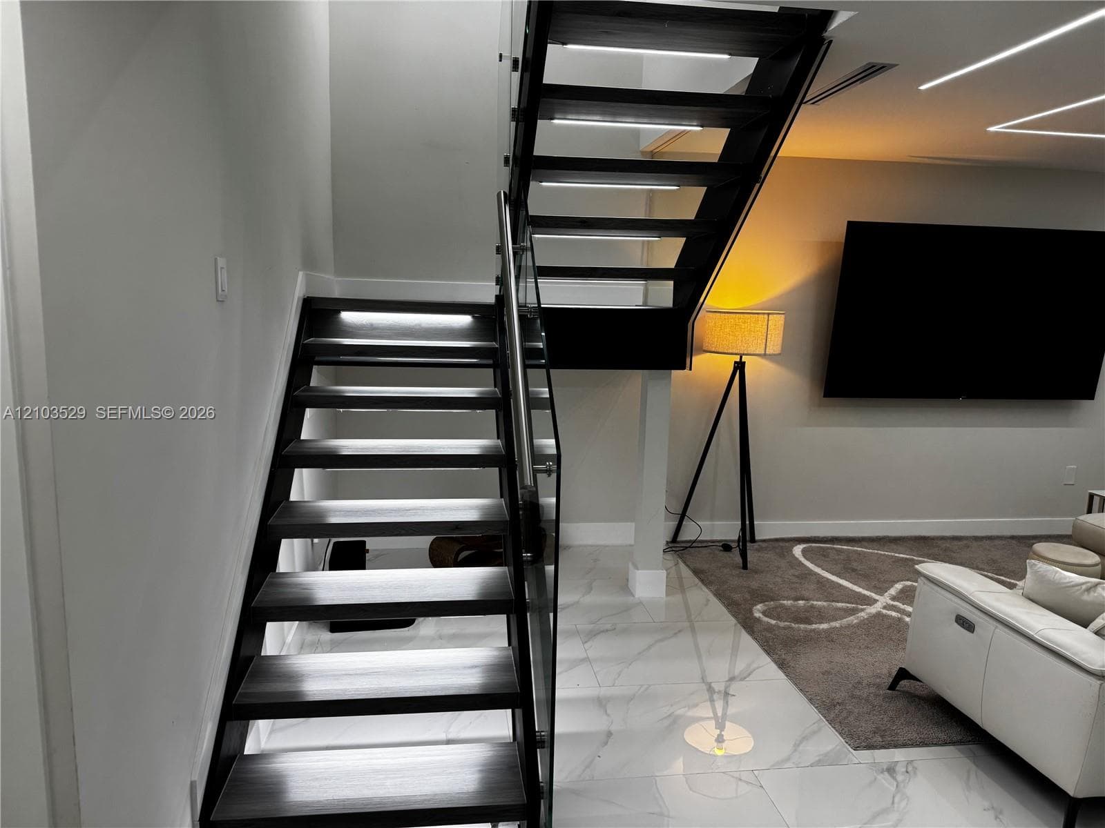 Open-riser staircase featuring dark wood-finish treads, integrated tread lighting, and a glass panel railing