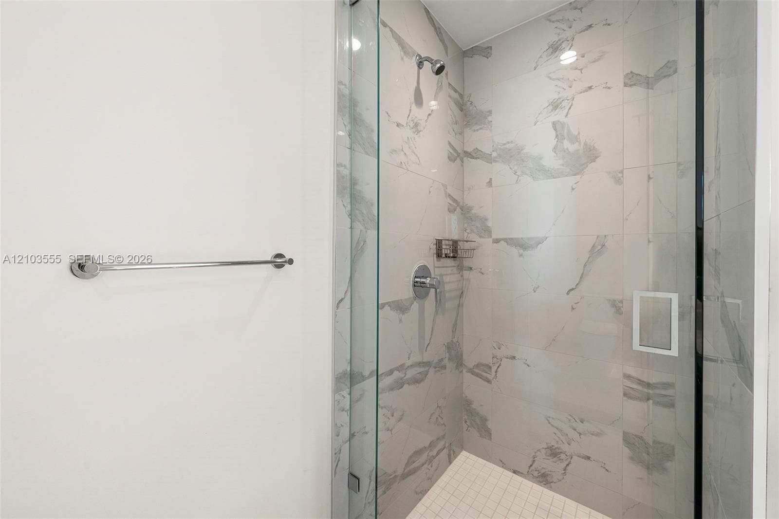 Shower enclosure featuring clear glass panels, a chrome shower head, a built-in soap niche, and white-patterned wall tiling
