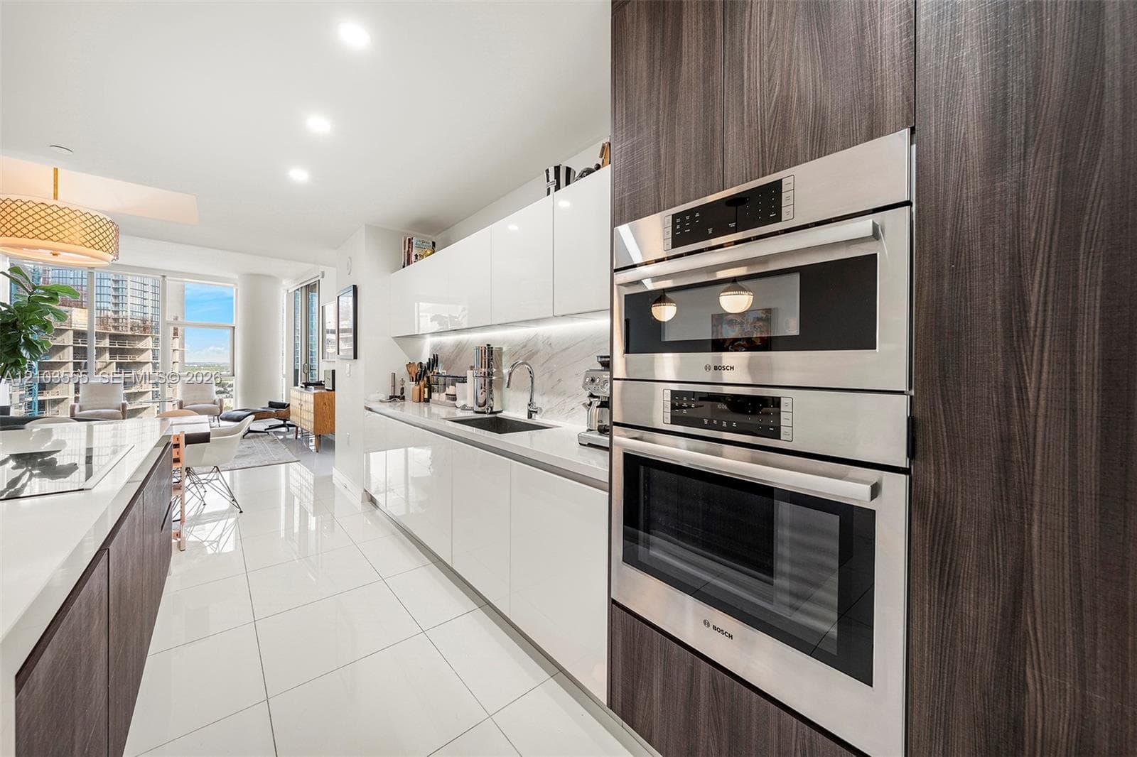 Sleek kitchen featuring integrated stainless steel appliances, dark wood-finish cabinetry, white high-gloss upper and lower cabinets, a white countertop, and white tile flooring
