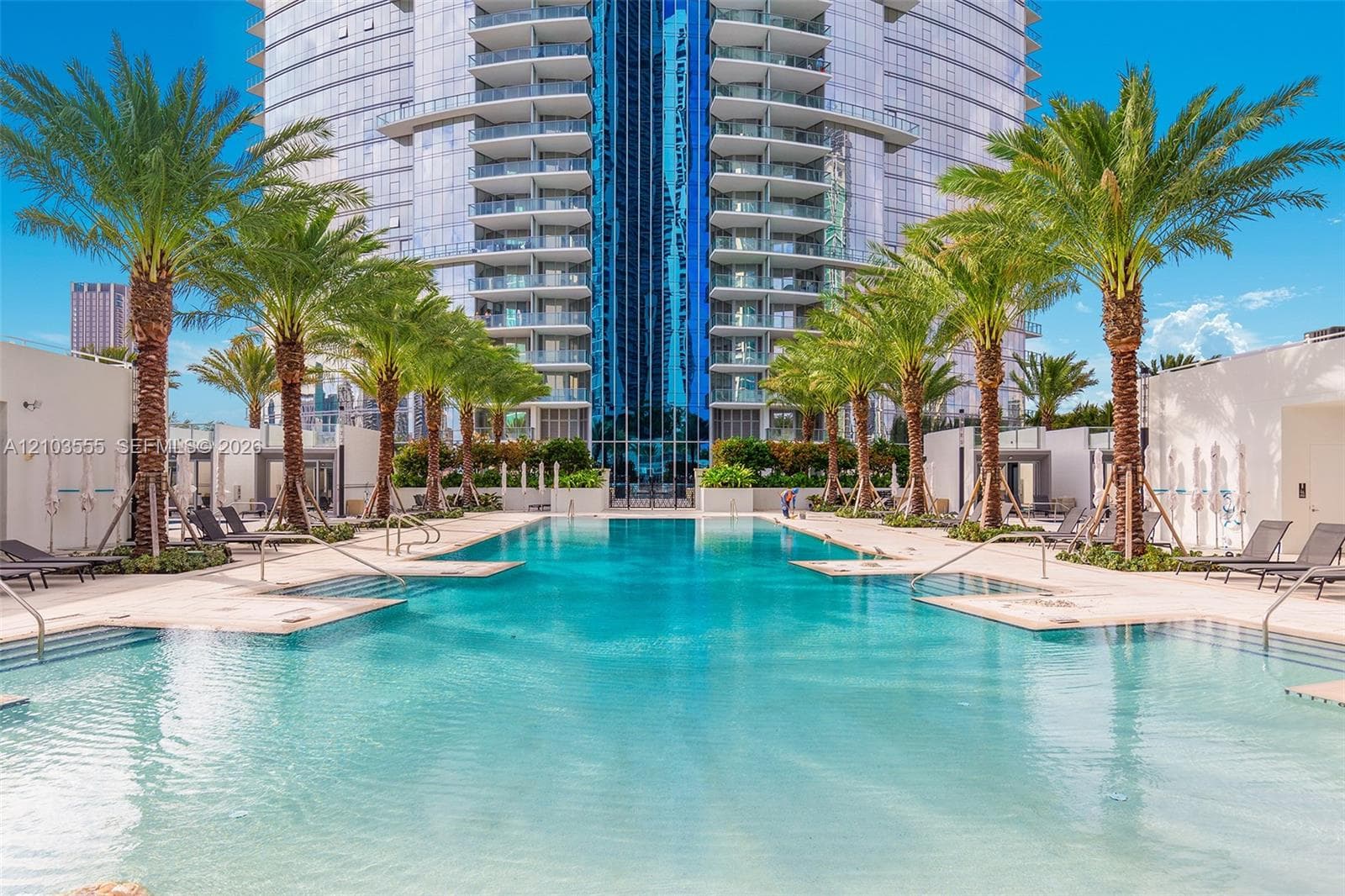 Expansive pool deck featuring multiple swimming pools, mature palm trees, and modern high-rise architecture