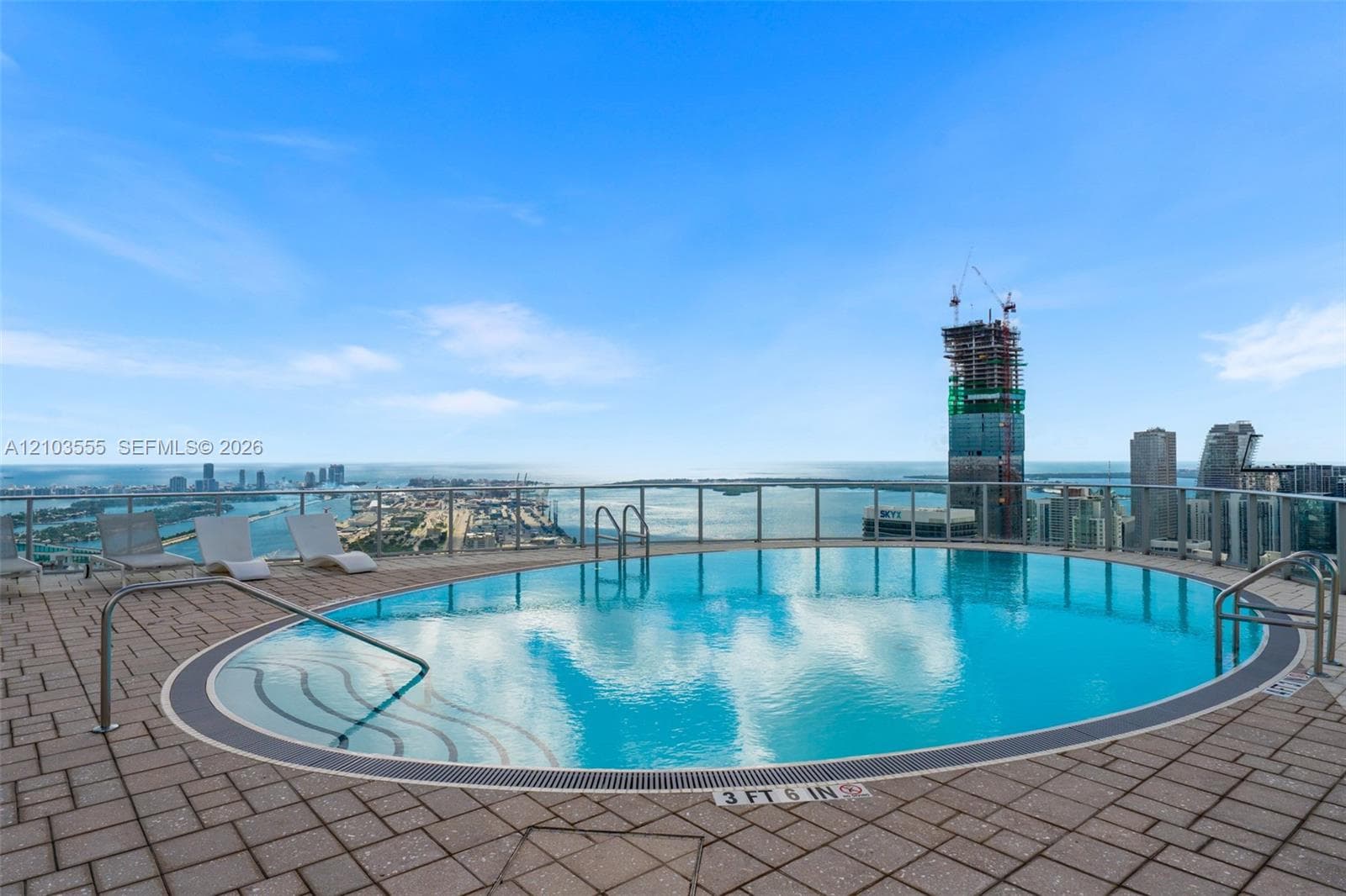 Rooftop swimming pool with an urban skyline backdrop, clear blue water, and a glass safety railing