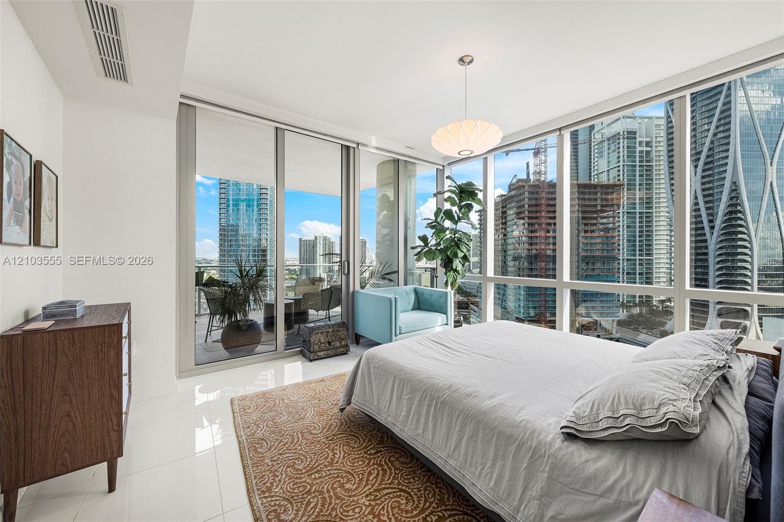 Floor-to-ceiling windows, polished tile flooring, sliding glass door to a private balcony, and a contemporary pendant light fixture