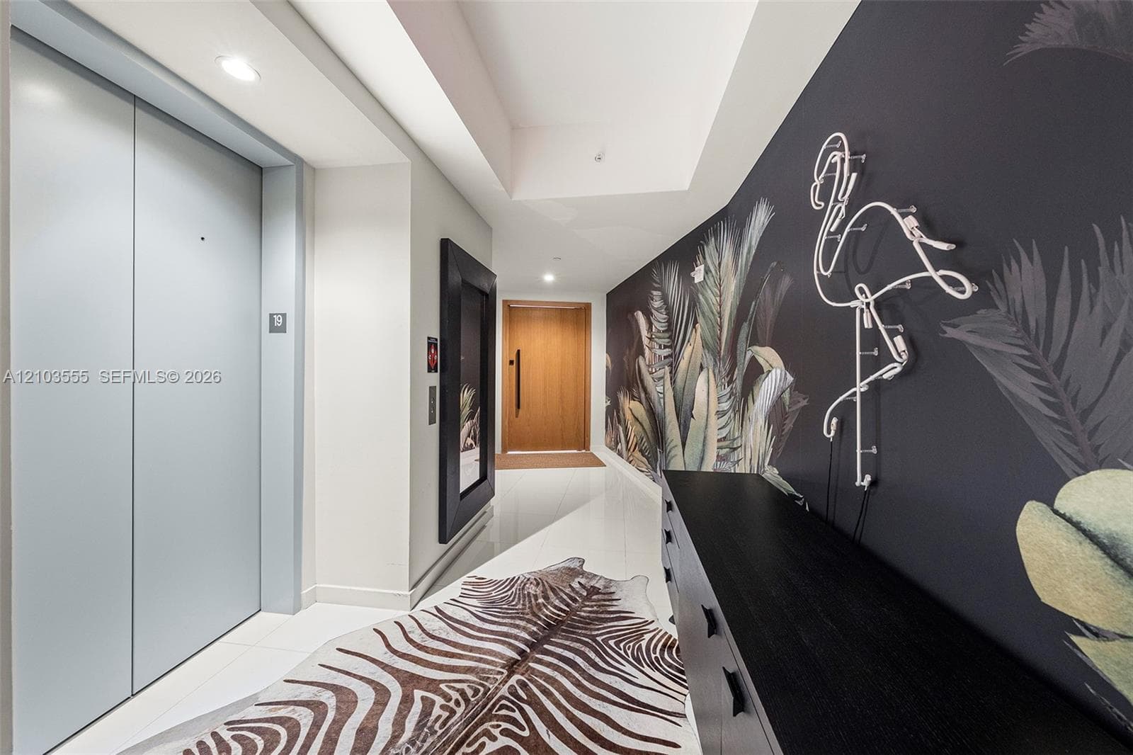 Recessed lighting illuminates the hallway with light-colored flooring, leading to a natural wood-finish door