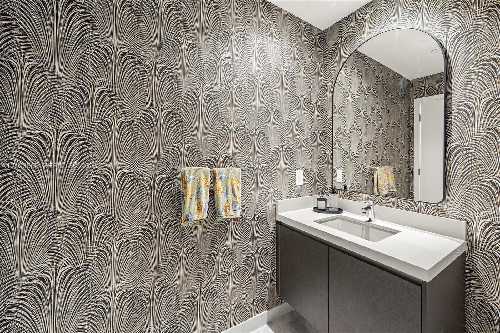 Patterned wallpaper, contemporary vanity with white countertop, integrated rectangular sink, wall-mounted curved mirror, and polished chrome faucet
