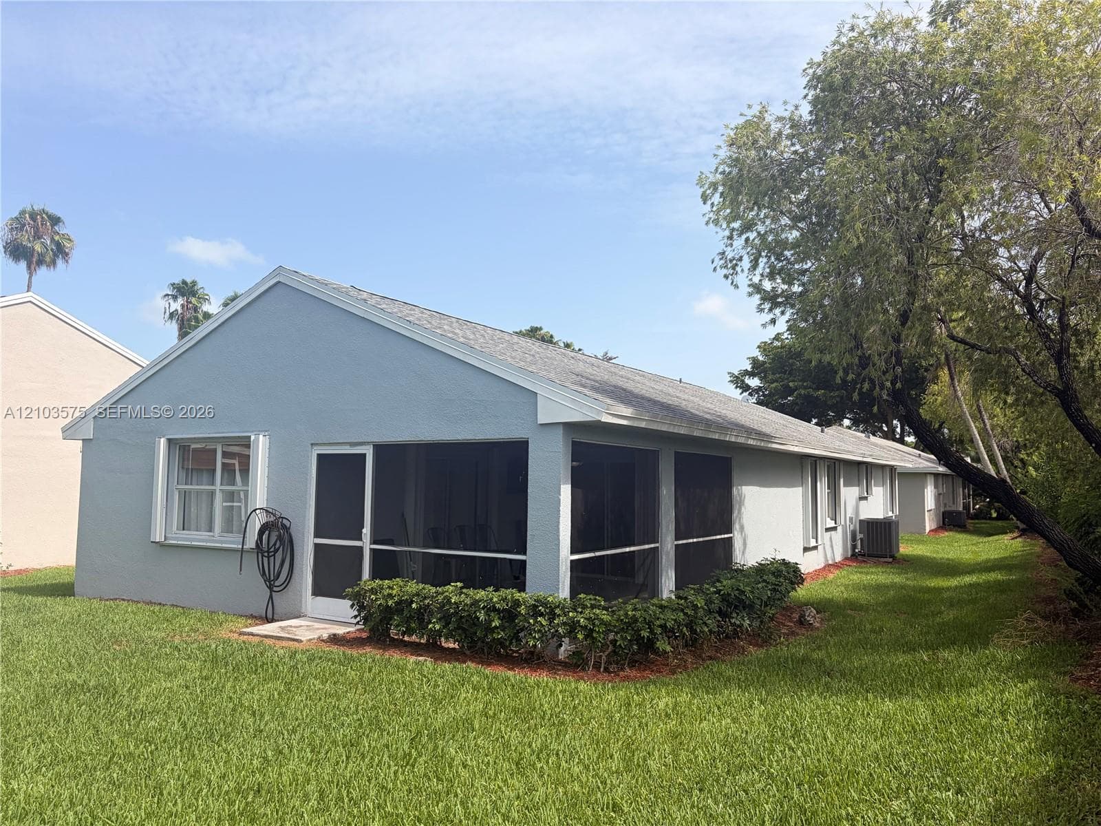 Exterior featuring a light-toned stucco finish, asphalt shingle gable roof, and an enclosed screened-in patio area