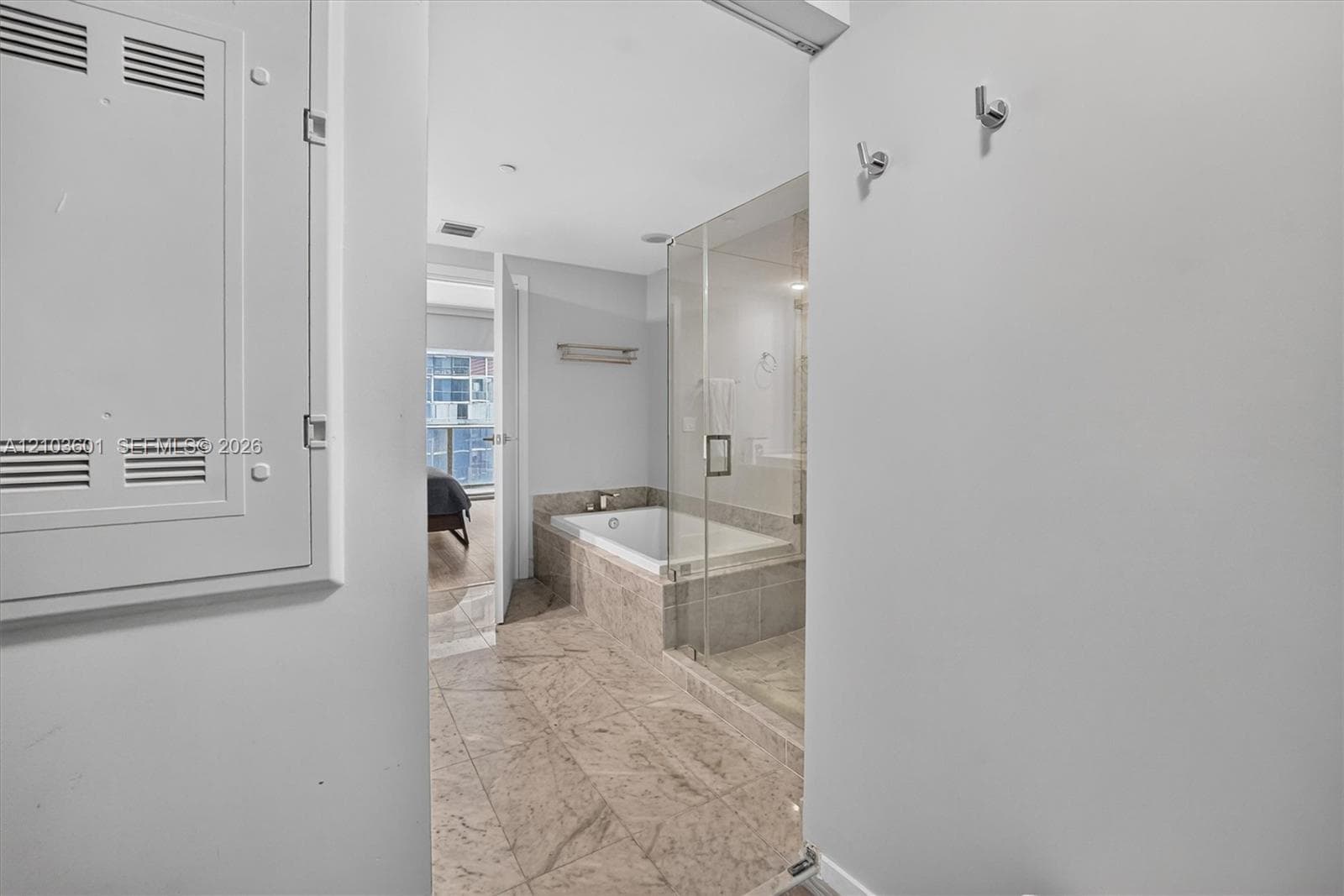 Bathroom featuring a drop-in soaking tub, a glass-enclosed shower, stone-finish tile flooring, and wall-mounted metal hooks