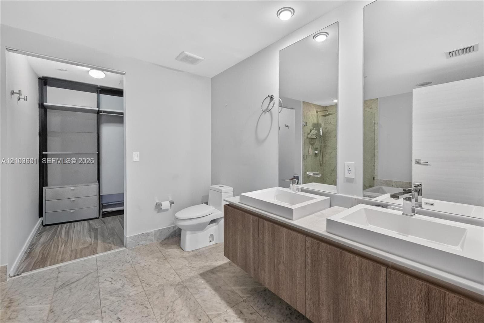 Floating double vanity with rectangular sinks, stone-finish floor tiling, recessed lighting, and integrated walk-in closet shelving