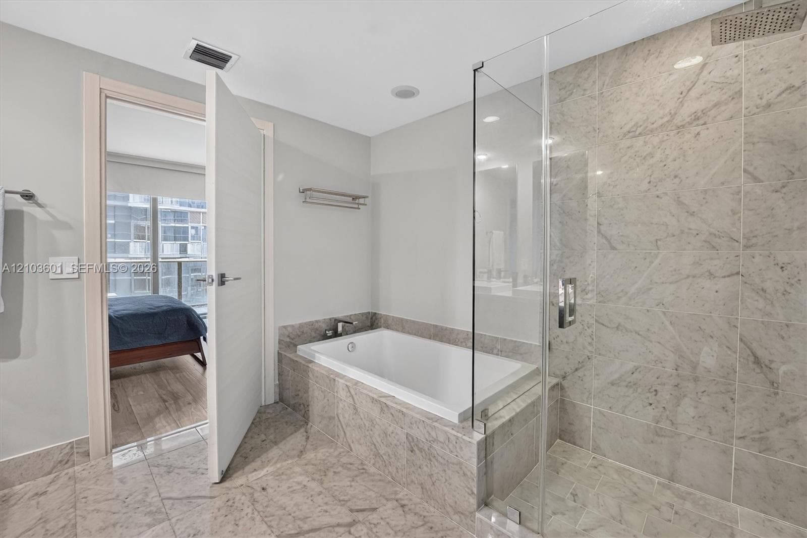 Bathroom featuring large-format stone tile flooring, a soaking tub with stone tile surround, and a walk-in shower enclosed by glass with a rainfall showerhead