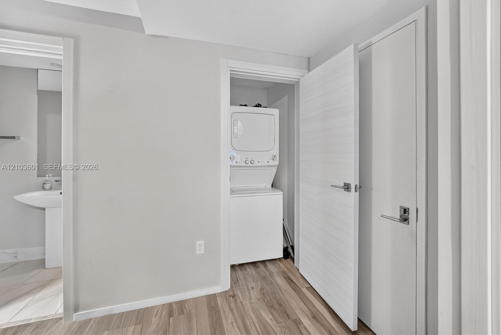 Laundry area featuring a stacked washer and dryer, wood-finish flooring, and minimalist slab-style interior doors with brushed metal hardware