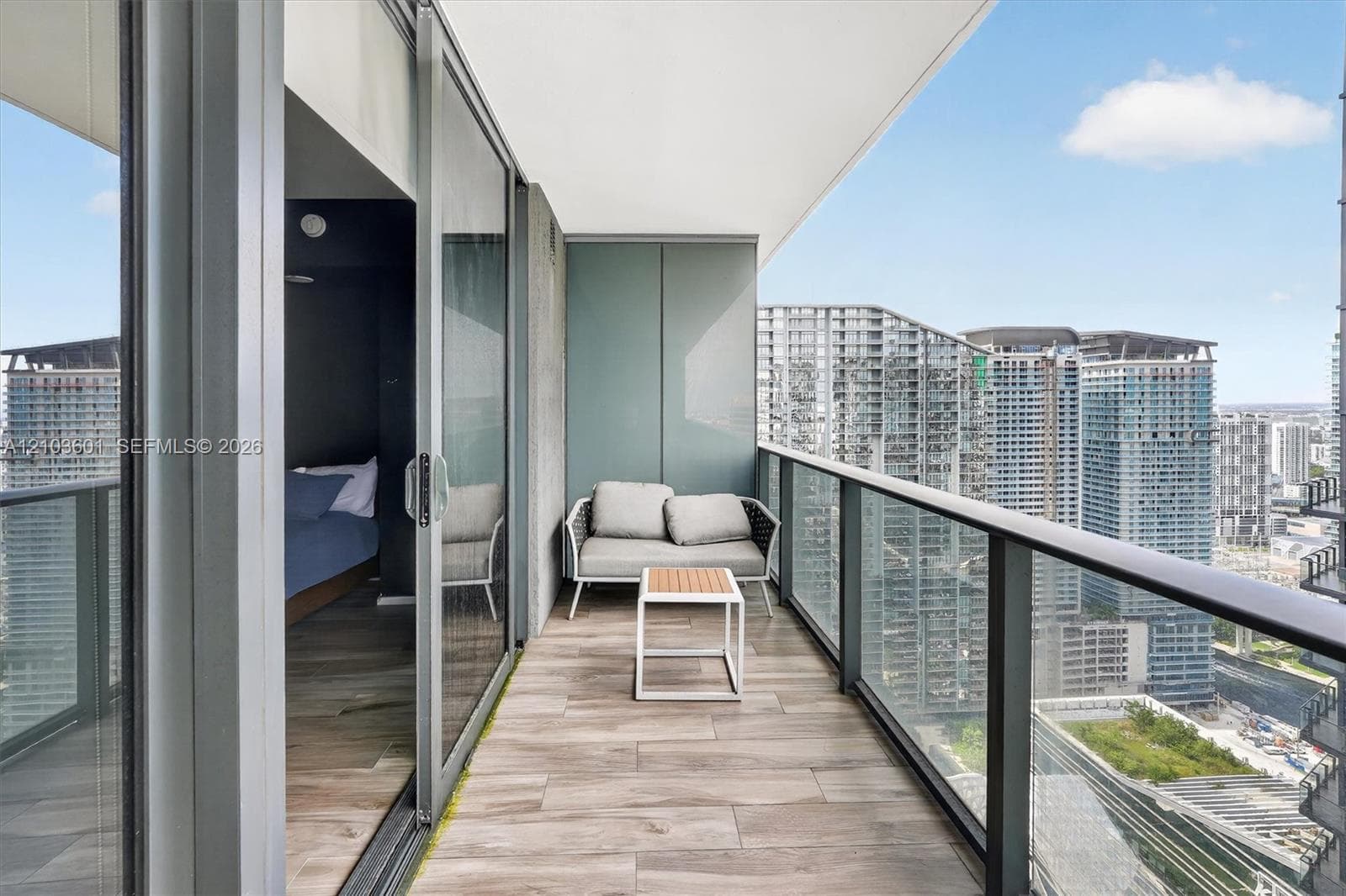 Covered balcony featuring wood-finish tile flooring, glass panel railing, and sliding glass door access