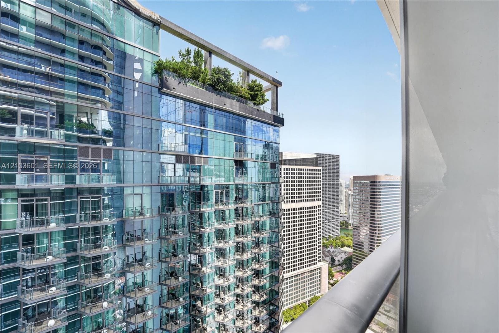 Private balcony featuring a glass panel railing and elevated exterior perspective of a glass-clad skyscraper with a rooftop garden