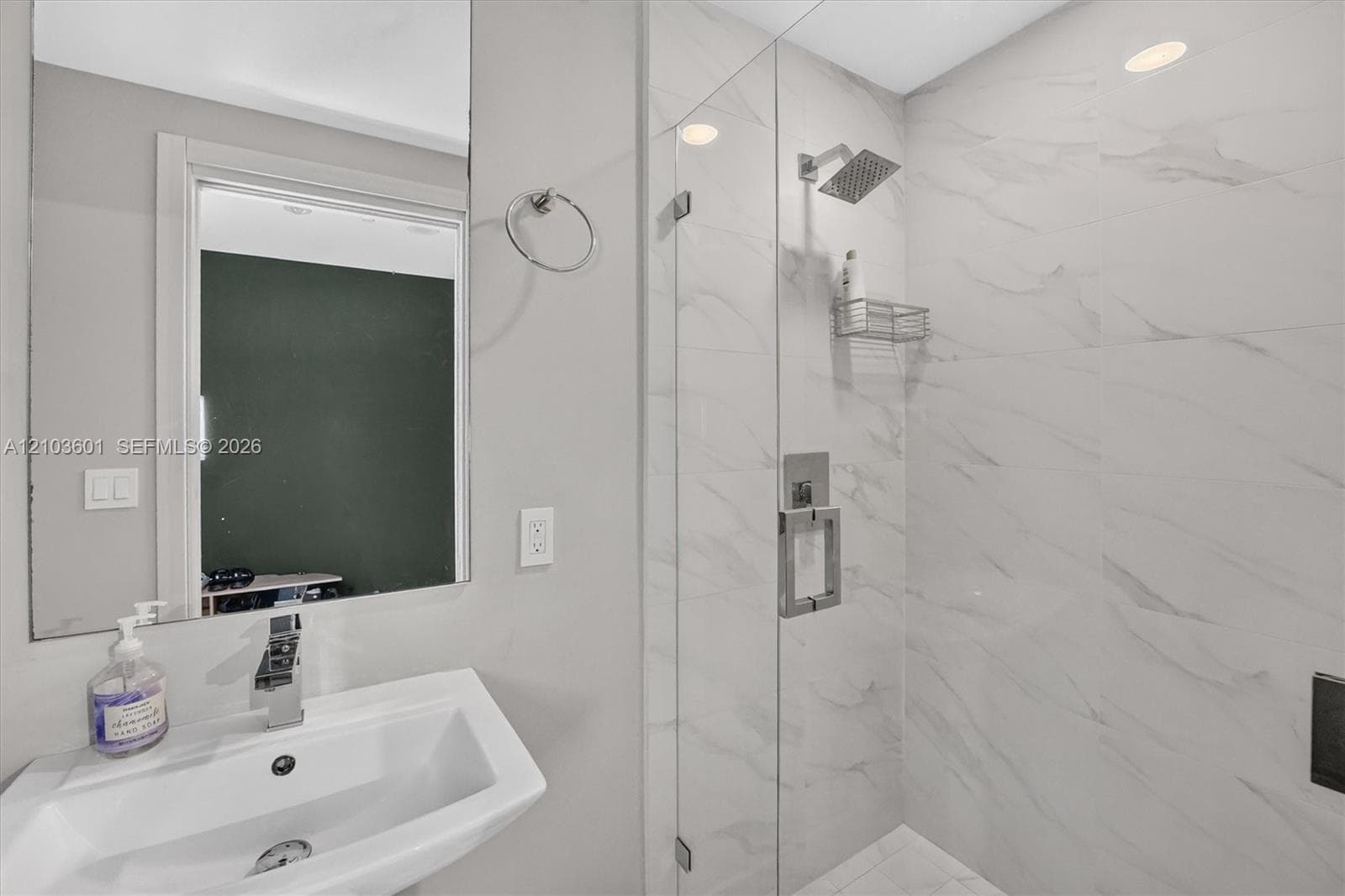Wall-mounted vanity with rectangular sink, frameless glass shower enclosure, and stone-finish wall tile