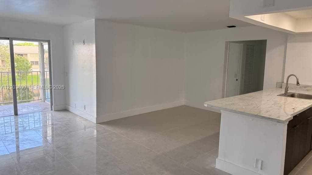 Kitchen island featuring stone-finish countertops, stainless steel sink, polished tile flooring, and sliding glass door with balcony access