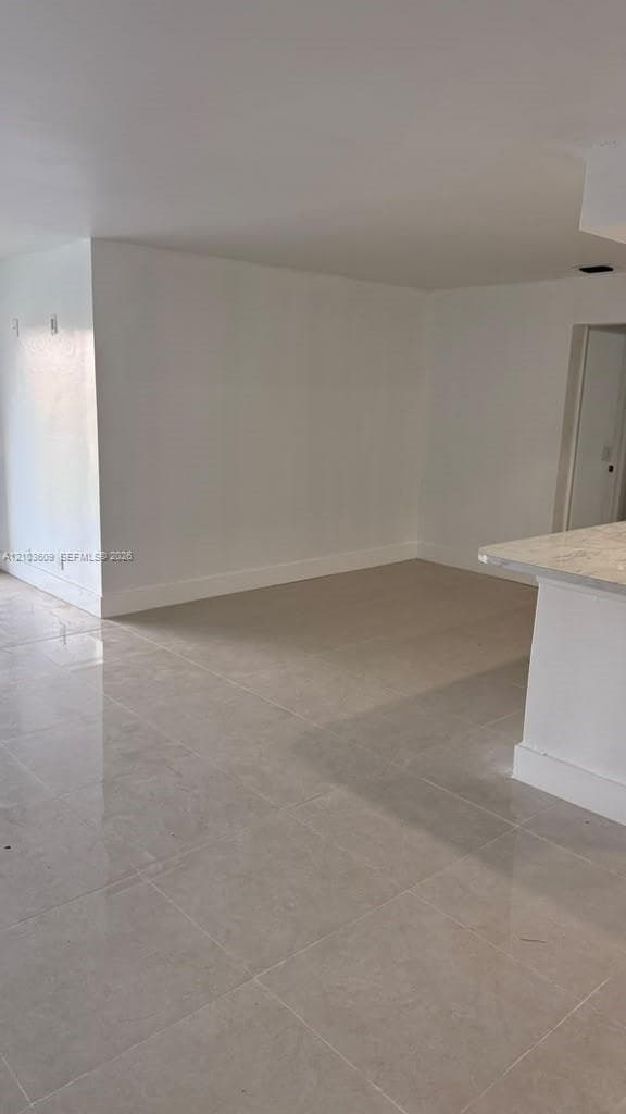 Interior space featuring polished stone-finish tile flooring, neutral wall tones, and a breakfast bar with a stone-surface countertop