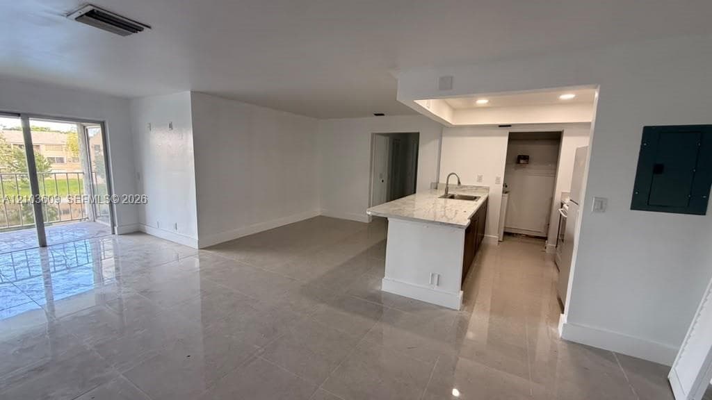 Open-concept interior featuring large-format tile flooring, a kitchen island with stone-finish countertops, recessed lighting, and sliding glass doors