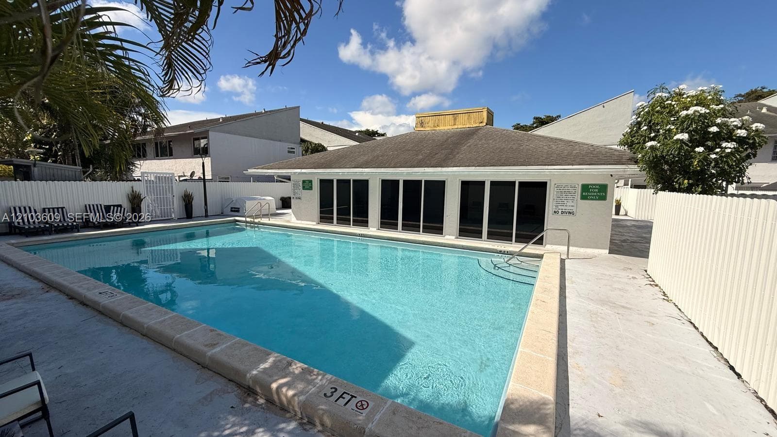 Swimming pool with stone coping, metal safety railings, and perimeter privacy fencing