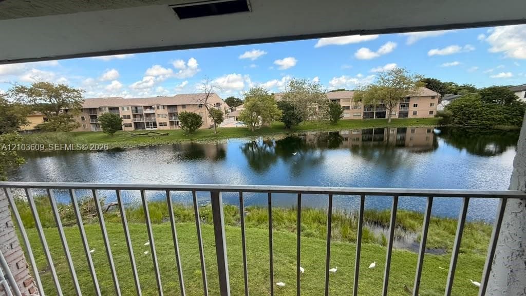 Covered balcony with a vertical metal railing overlooking a pond and landscaped green space