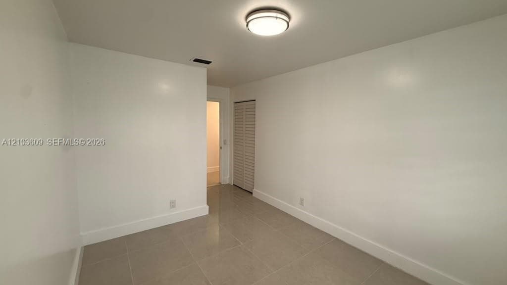 Neutral interior space featuring polished tile flooring, crisp white walls, a flush-mount circular ceiling light, and a bi-fold louvered closet door