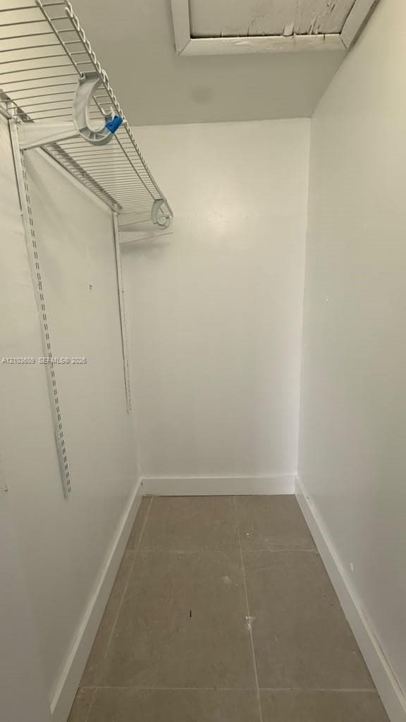 Storage space featuring ceramic tile flooring and white walls, equipped with wire shelving and an attic access panel
