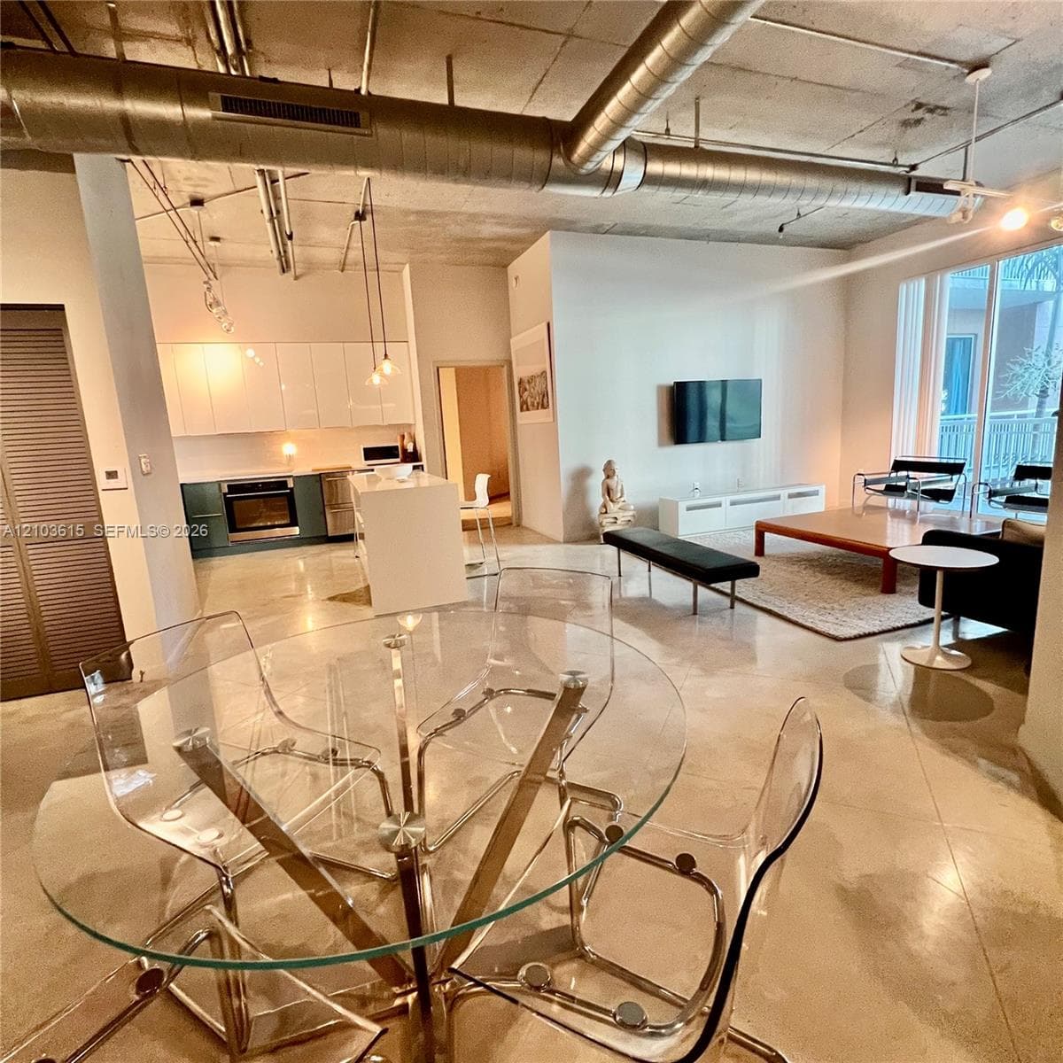 Industrial-style loft interior featuring exposed concrete ceilings with prominent metal ductwork, polished concrete flooring, white flat-panel cabinetry, and a central kitchen island