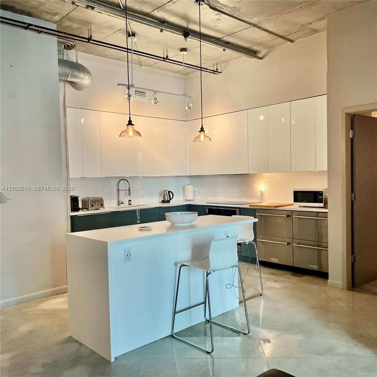 Industrial-style kitchen featuring exposed concrete ceilings, high-gloss white upper cabinetry, a central island with a solid-surface countertop, stainless steel integrated appliances, and polished concrete flooring