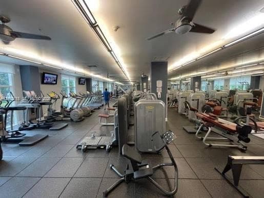 Fitness center featuring rubber flooring, recessed ceiling lighting, wall-mounted televisions, and multiple ceiling fans