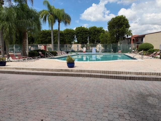 Swimming pool with a surrounding paved deck, brick-patterned steps, and mature palm trees