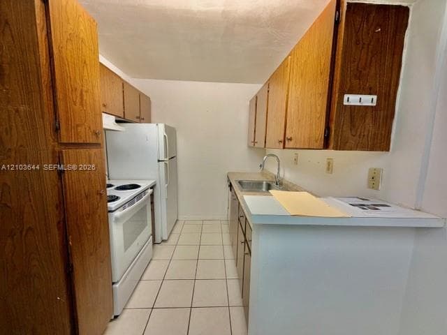 Galley kitchen with wood-finish cabinetry, white appliances, and tiled flooring