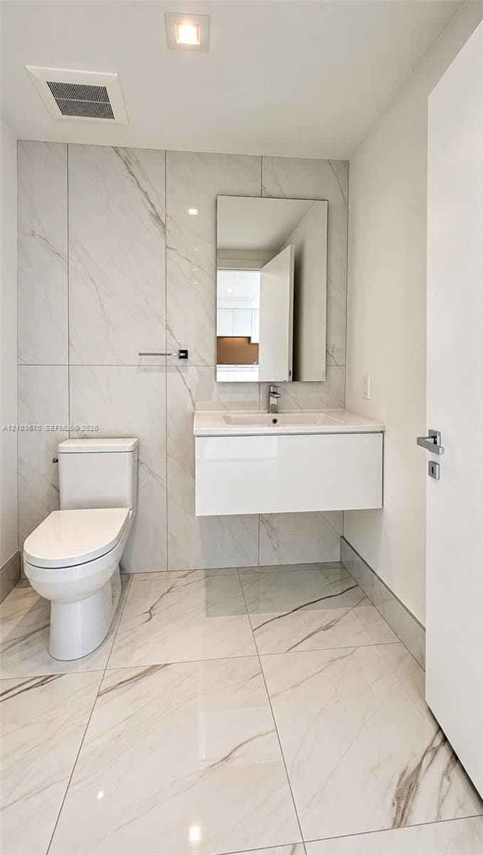 Floating vanity with a white integrated basin, floor-to-ceiling large-format tile wall, white stone-patterned floor tiling, rectangular mirror, and chrome single-handle faucet
