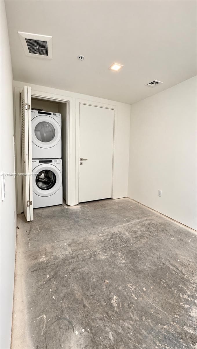 Stacked laundry unit with white appliances, enclosed within a closet featuring bi-fold doors, complemented by recessed ceiling lighting and a flat-panel interior door