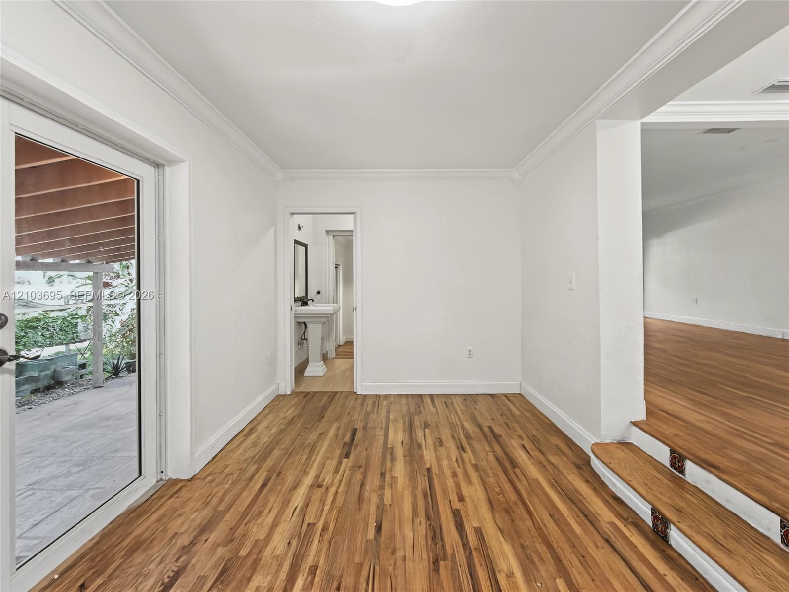 Wood-finish flooring, crown molding, glass-paned exterior door, and elevated platform featuring decorative tile accents