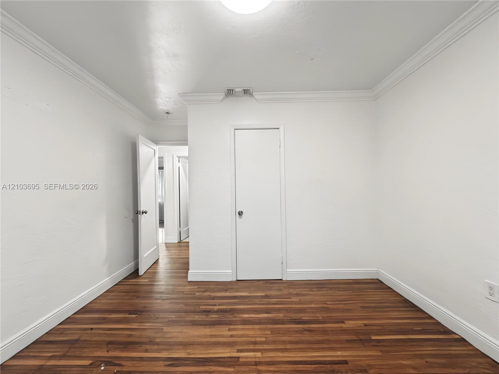 Interior space featuring wood-finish flooring, crisp white walls, crown molding, and solid-core interior doors with metallic hardware