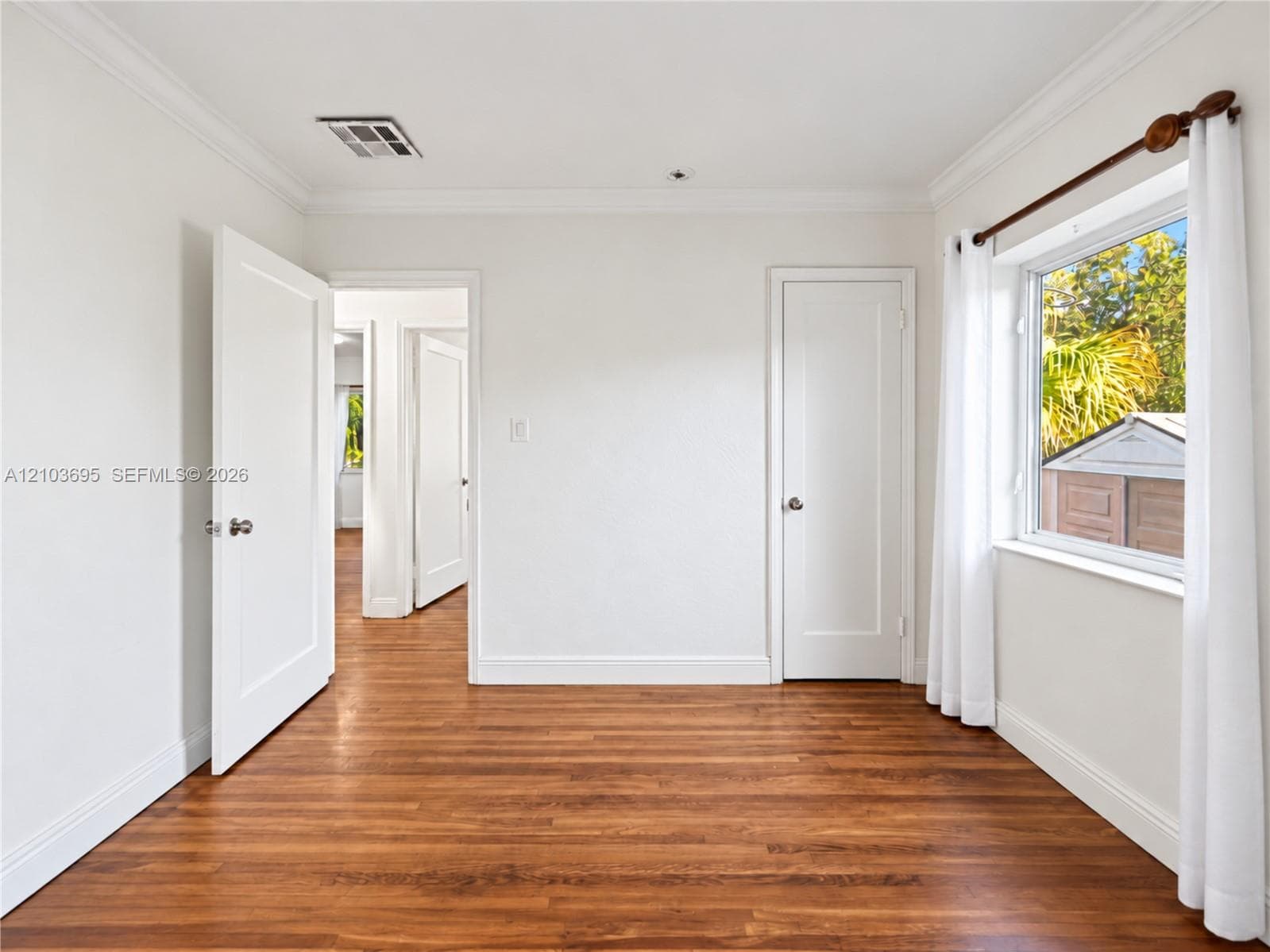 Interior space featuring wood-finish flooring, crown molding, white shaker-style doors, and natural light through a side window