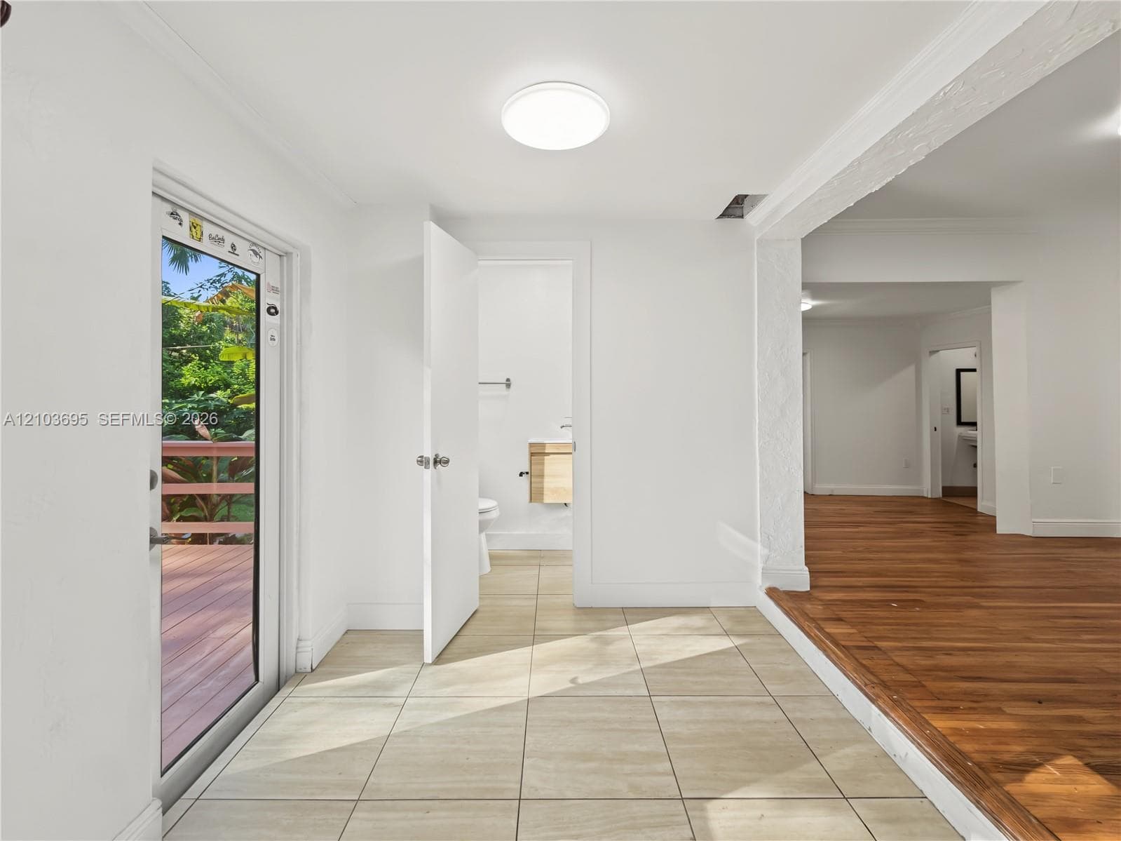 Interior space featuring large-format neutral floor tiling, wood-finish flooring, crown molding, a flush-mount ceiling light fixture, and a glass-paneled exterior door