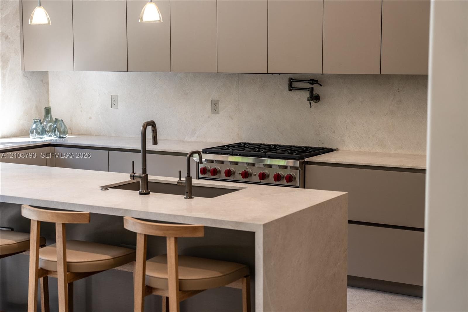 Kitchen featuring flat-panel cabinetry, a waterfall-edge stone island with an integrated sink and gooseneck faucet, a professional-style gas range, and a wall-mounted pot filler