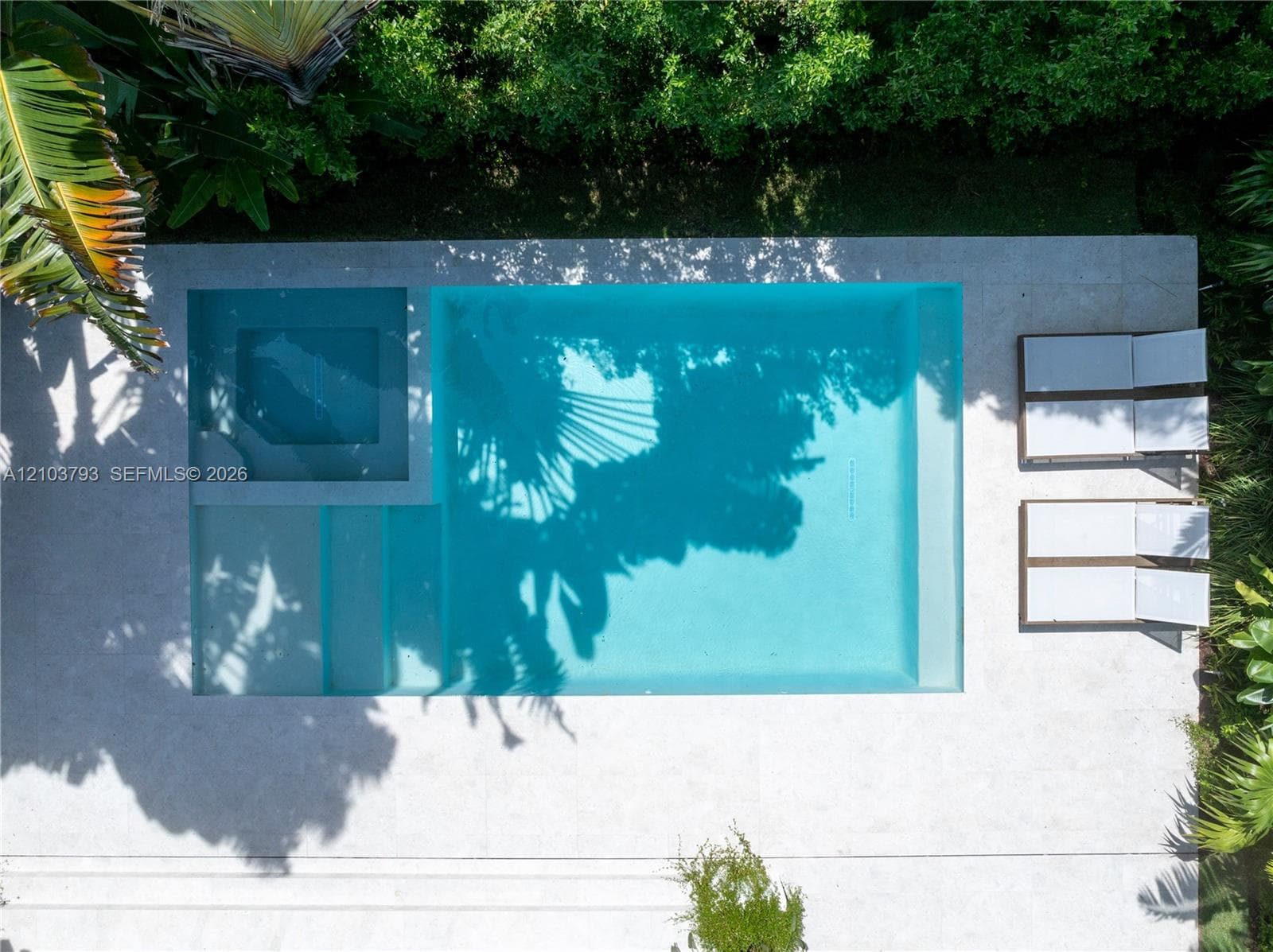Aerial view of residential property featuring a clay tile roof, a rectangular swimming pool, a concrete patio, and mature perimeter landscaping