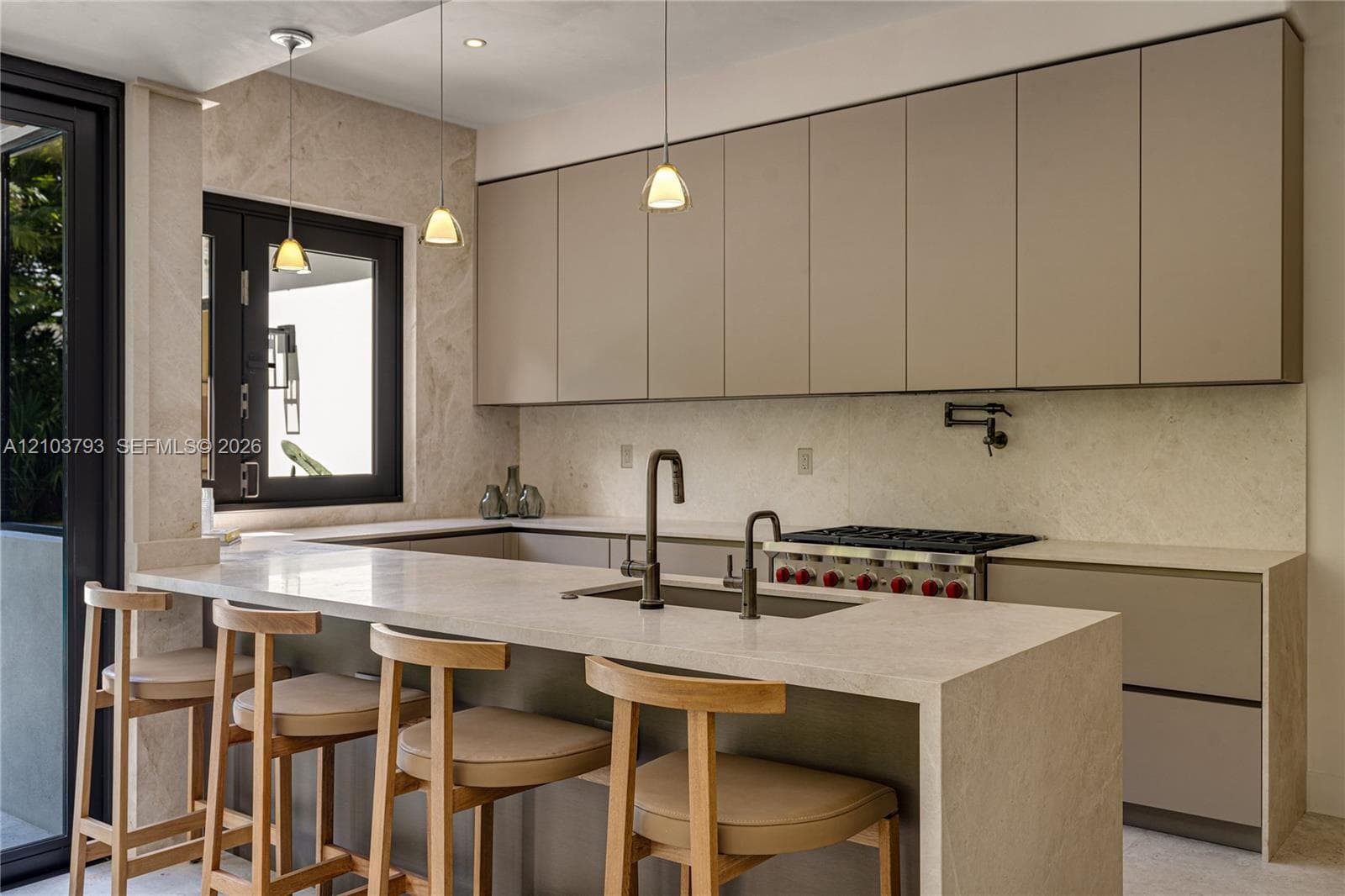 Modern kitchen featuring flat-panel cabinetry, a waterfall-edge countertop, stone wall cladding, a wall-mounted pot filler, and recessed pendant lighting