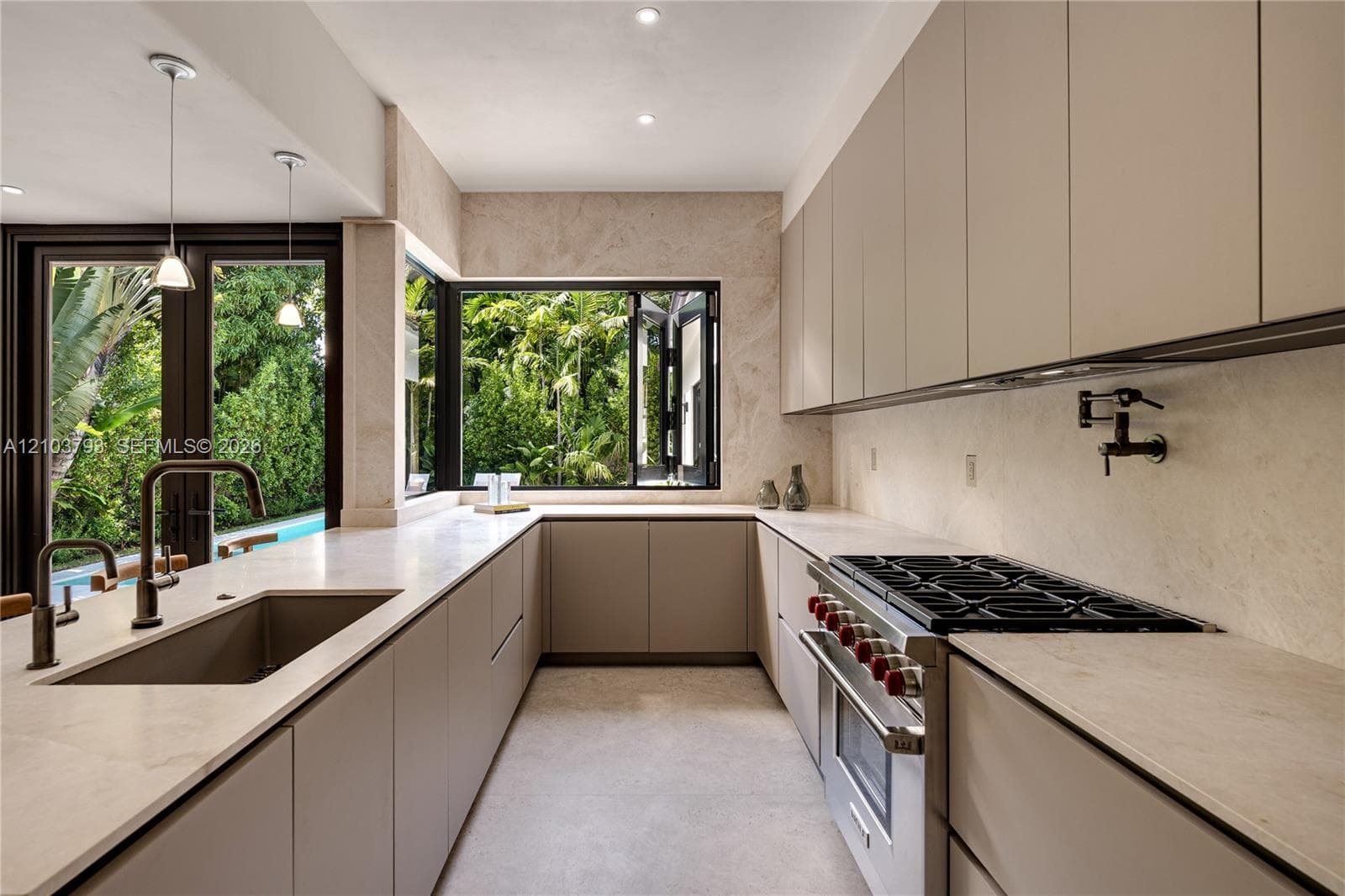 Kitchen featuring matte-finish flat-panel cabinetry, light-toned stone countertops, a stainless steel gas range with a wall-mounted pot filler, and metal pendant lighting